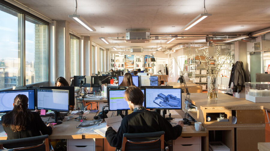 Multiple people sit at desks with large monitors in a busy and eclectic studio