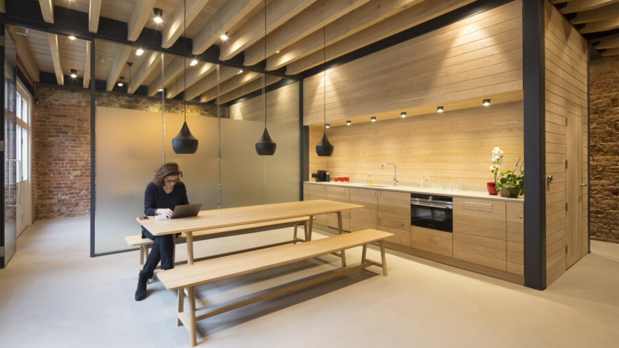 A woman sitting at a bench in a modern office kitchen area