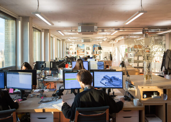 Multiple people sit at desks with large monitors in a busy and eclectic studio